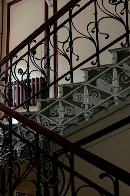 A staircase with a narrow, winding design featuring white-painted wooden steps and black decorative balusters, leading upward from a small landing. The staircase is enclosed by white brick walls, with